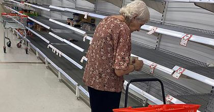 Woman stares at empty shelves as people continue to buy large amounts of toilet paper