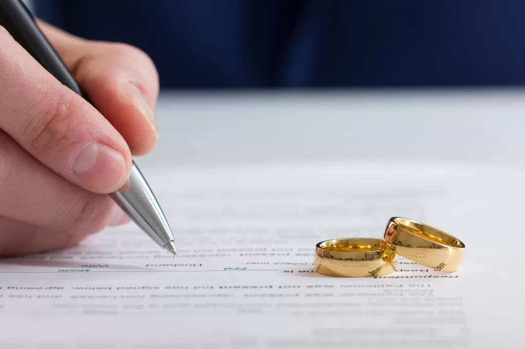 A person signing divorce papers with two gold rings resting nearby | Source: Shutterstock