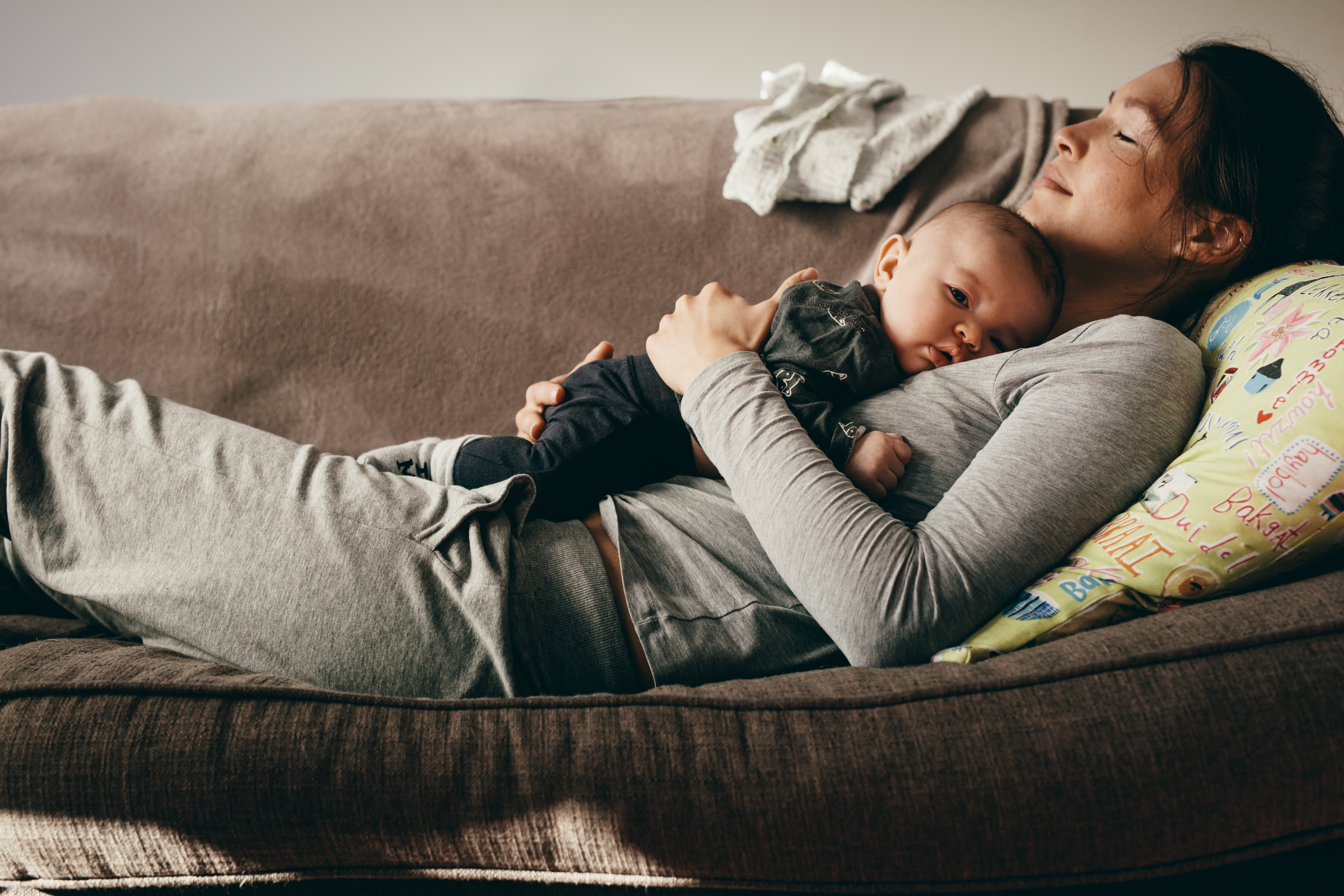 A mother laying on the couch while holding a baby | Source: Shutterstock