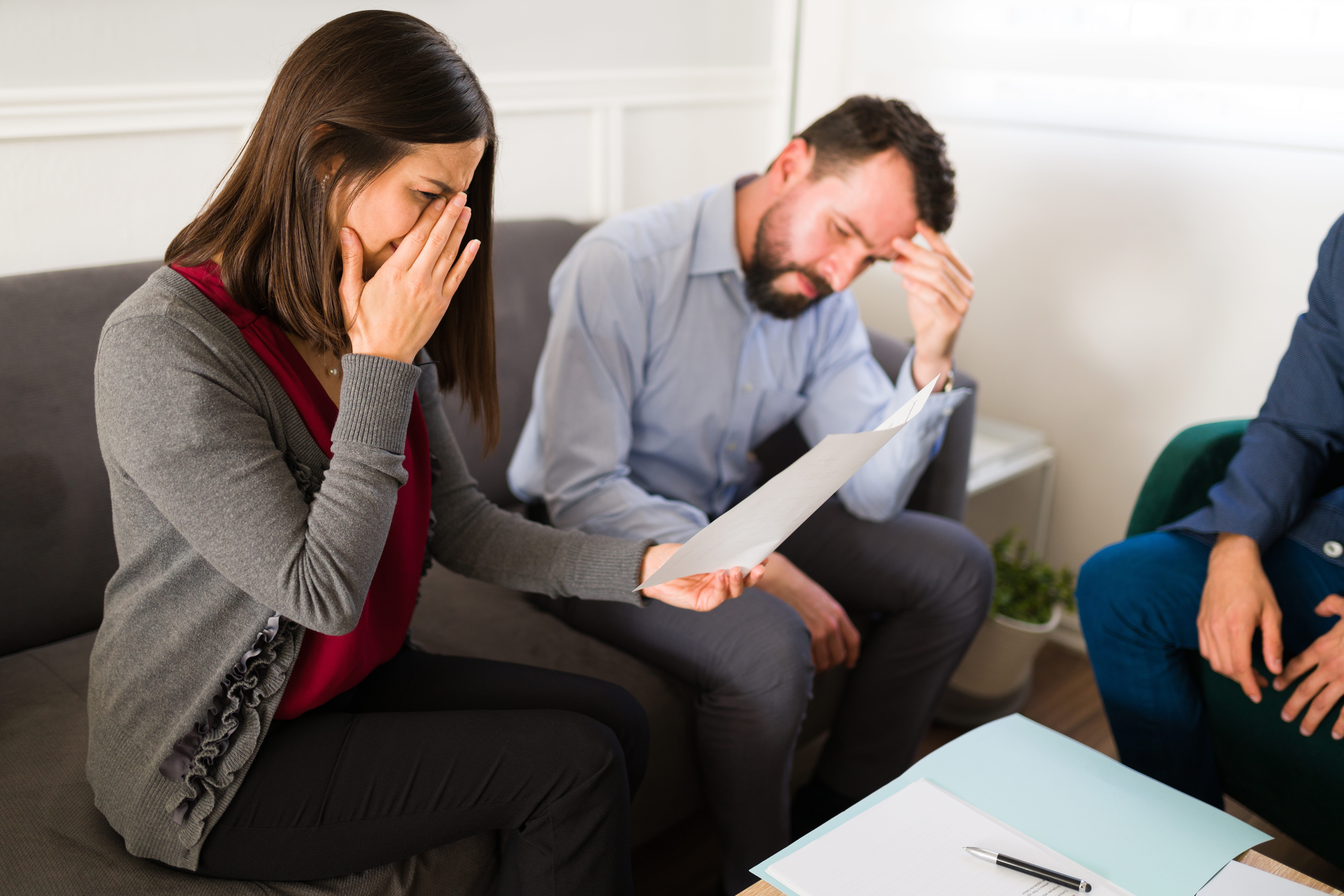 A woman crying while holding a piece of paper in her hand with a man sitting beside her | Source: Shutterstock