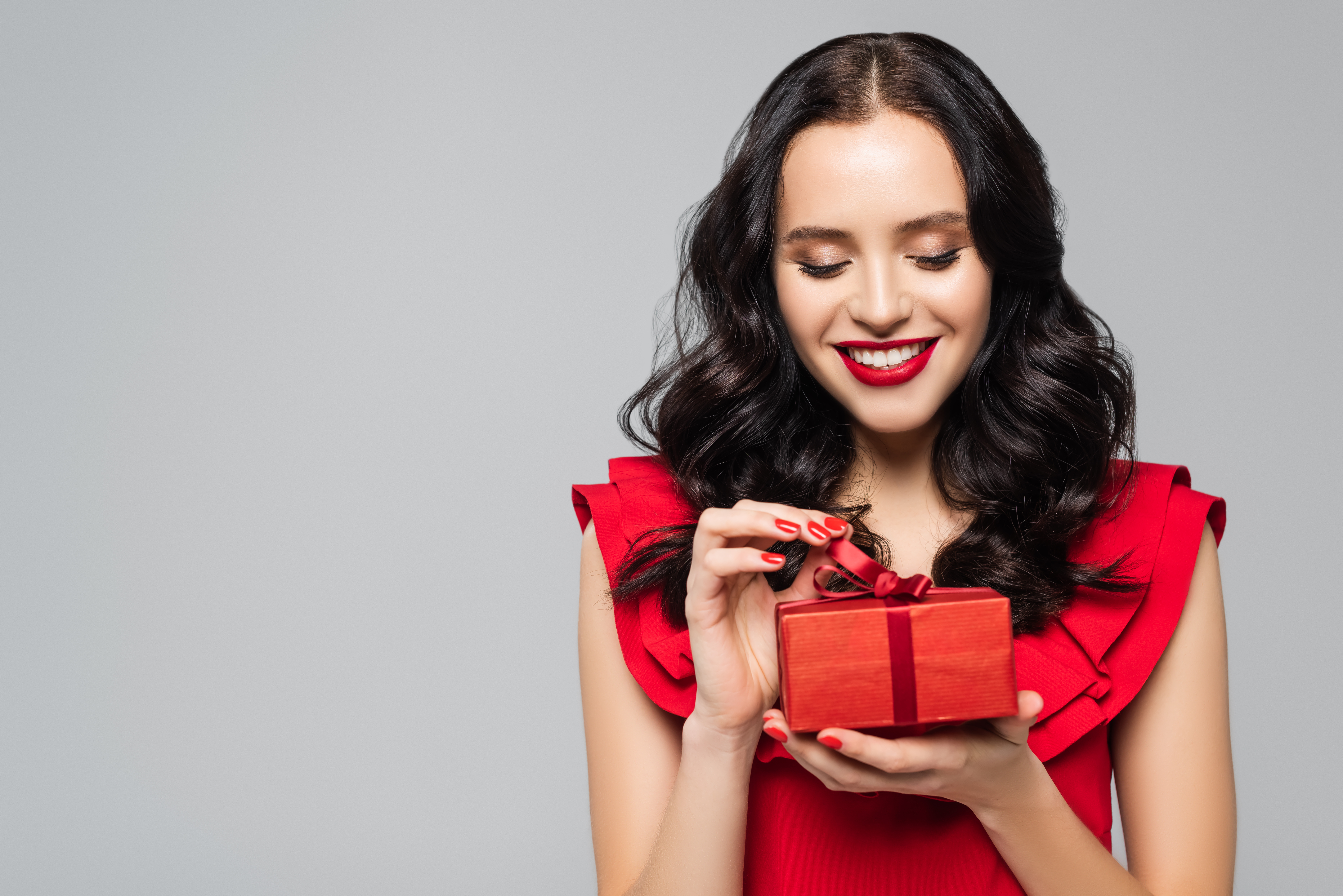 A cheerful woman in a red dress is seen holding a gift box | Source: Shutterstock