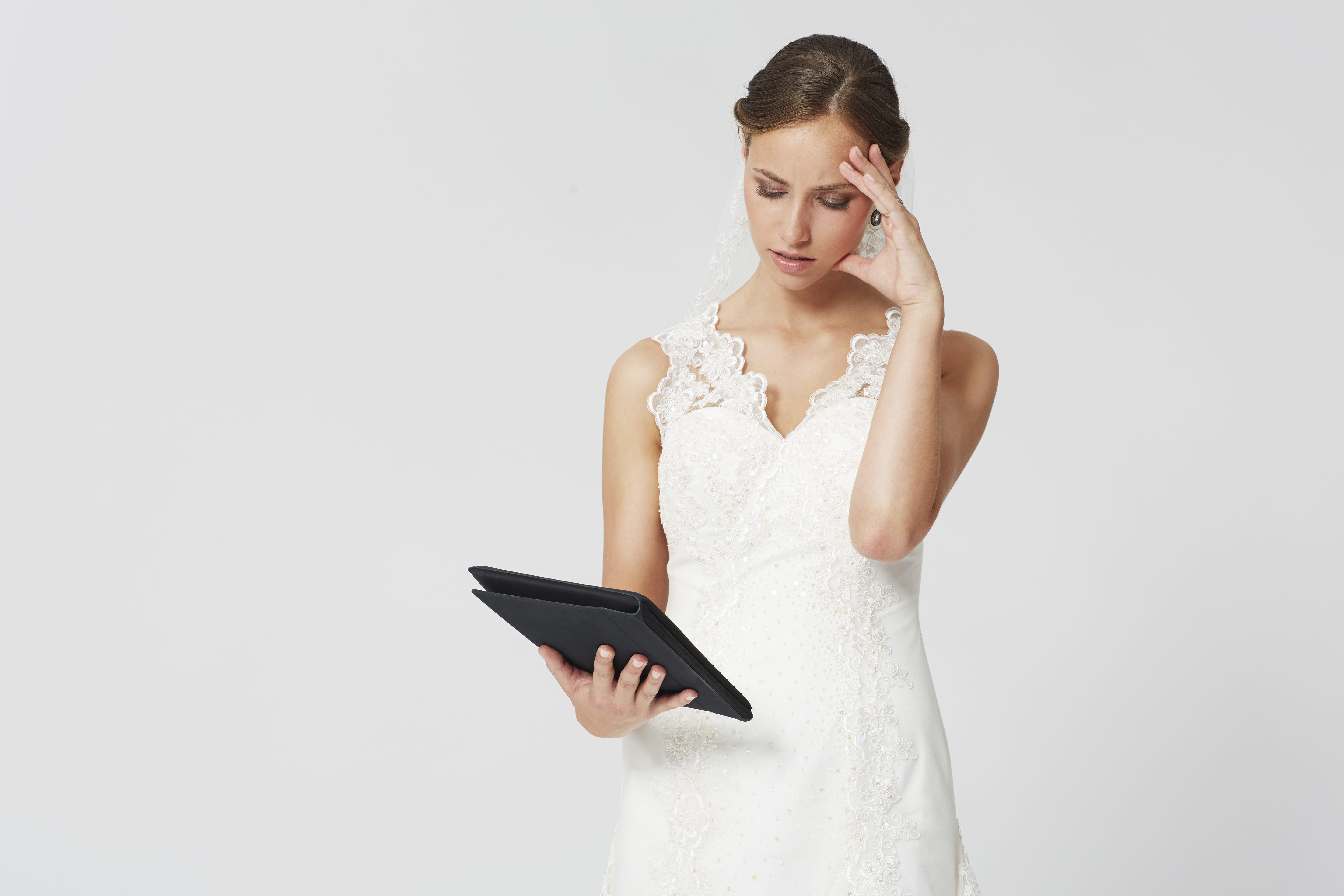 A woman in a white bridal dress looking confused while holding a tablet | Source: Shutterstock