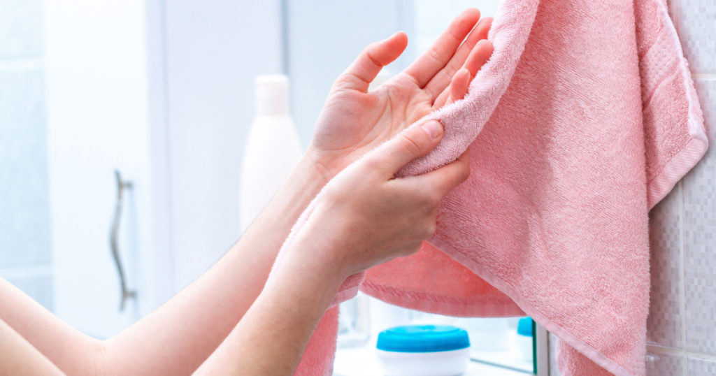 Person using towel for wiping hands dry after washing in bathroom at home. Hygiene and hand care
