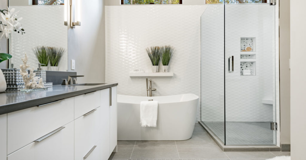 bright clean bathroom with white porcelain glass shower elegant tile grey cabinets basket weave tile on floor with access to laundry and walk in closet
