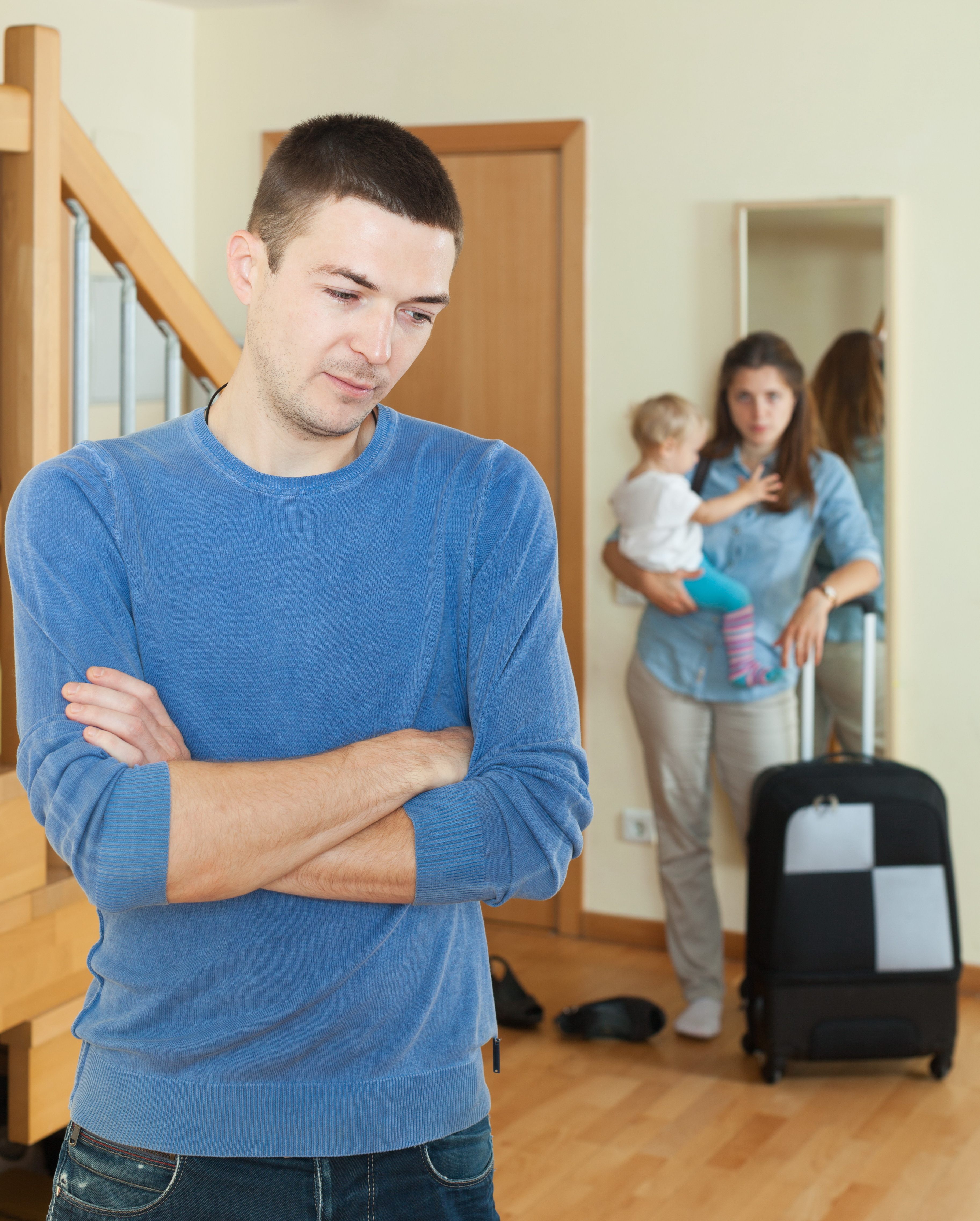 A woman with a suitcase and baby looking at a man with his back turned to her | Source: Shutterstock