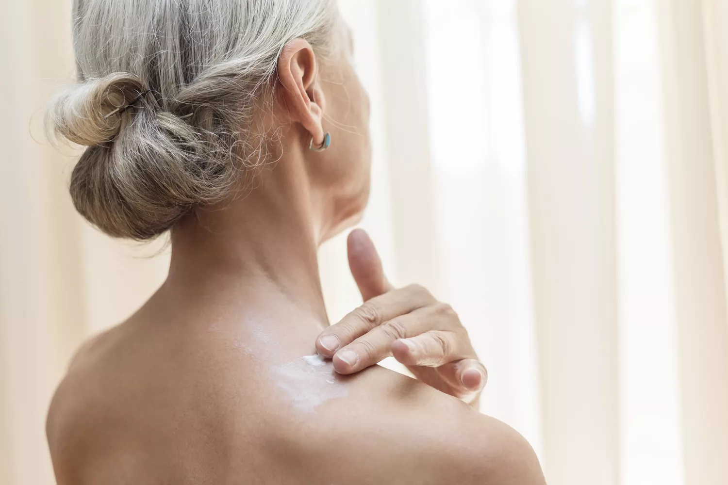 Back view of senior woman applying cream on neck