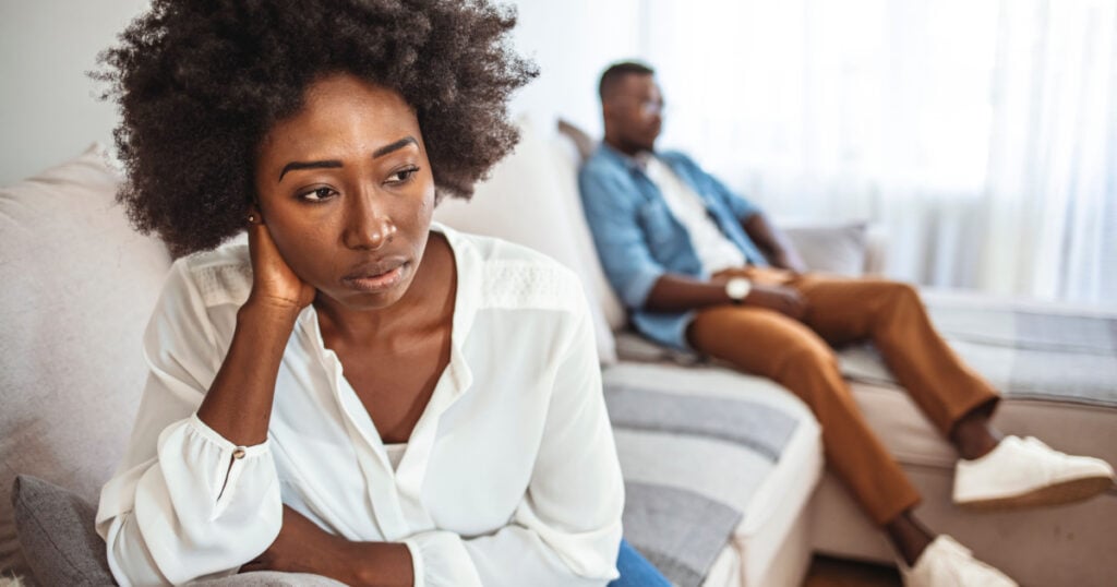 Upset couple at home. Handsome man and beautiful young woman are having quarrel. Sitting on sofa together. Family problems. I can't believe we're fighting about this again.
