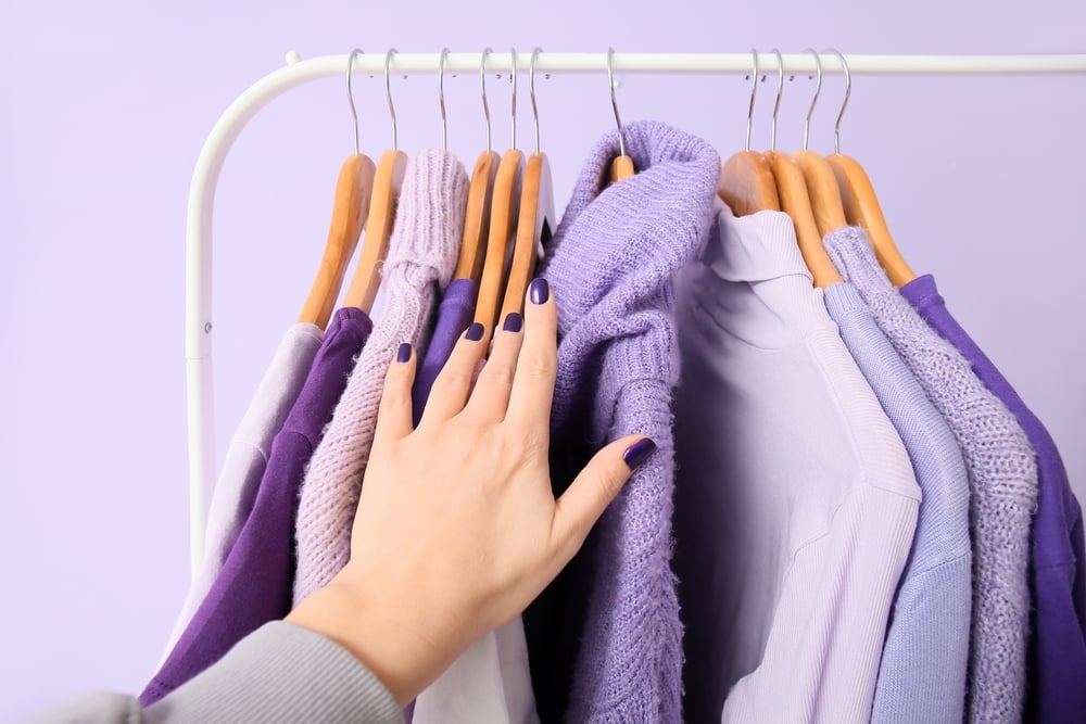 Woman and rack with clothes in purple shades on lilac background, closeup