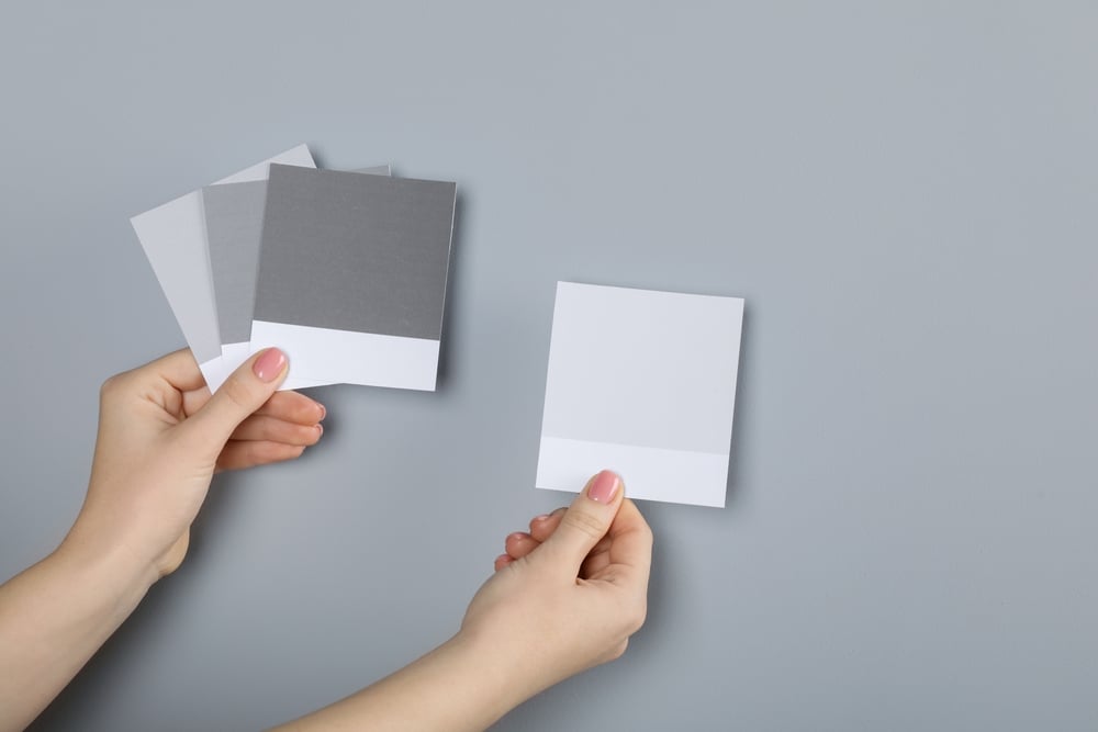 Woman with color sample cards choosing paint shade near grey wall, closeup. Interior design