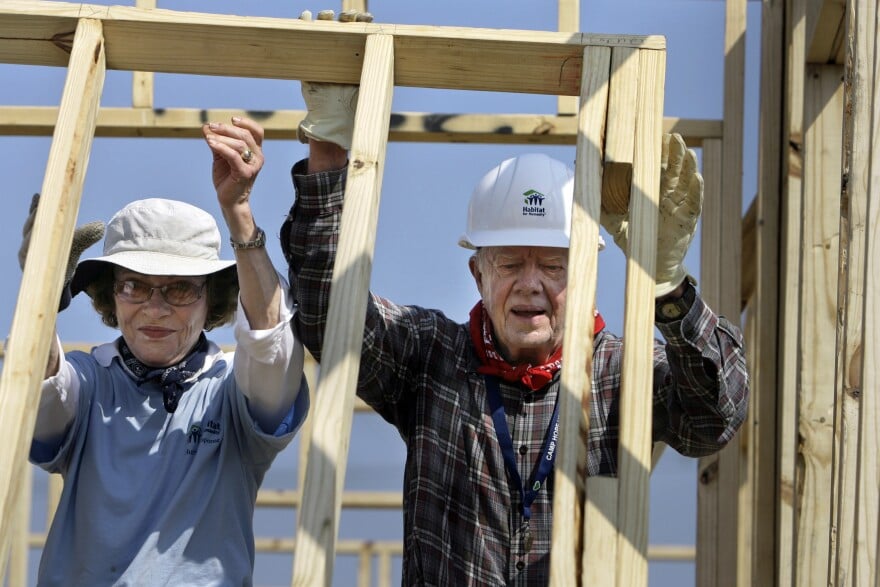 Jimmy Carter is on the right, next to his wife Rosalynn. They are seen building a house for Habitat for Humanity. 