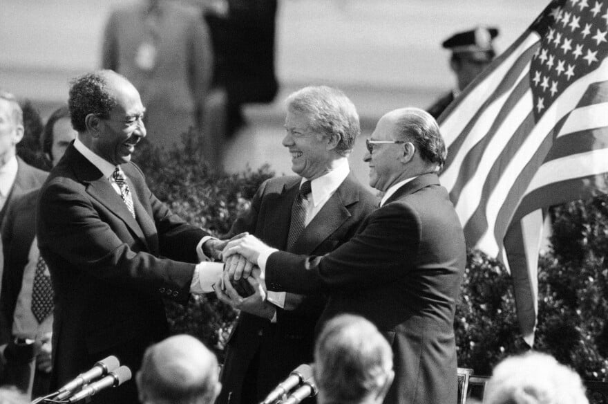 Jimmy Carter is in the center of three men in a black and white photo from 1979.