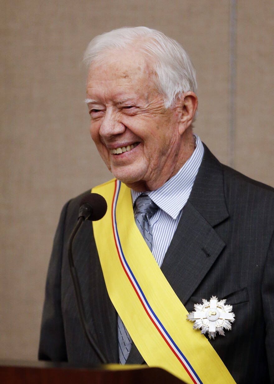 Jimmy Carter is seen wearing a yellow sash with a red, white and blue stripe down the middle of it.