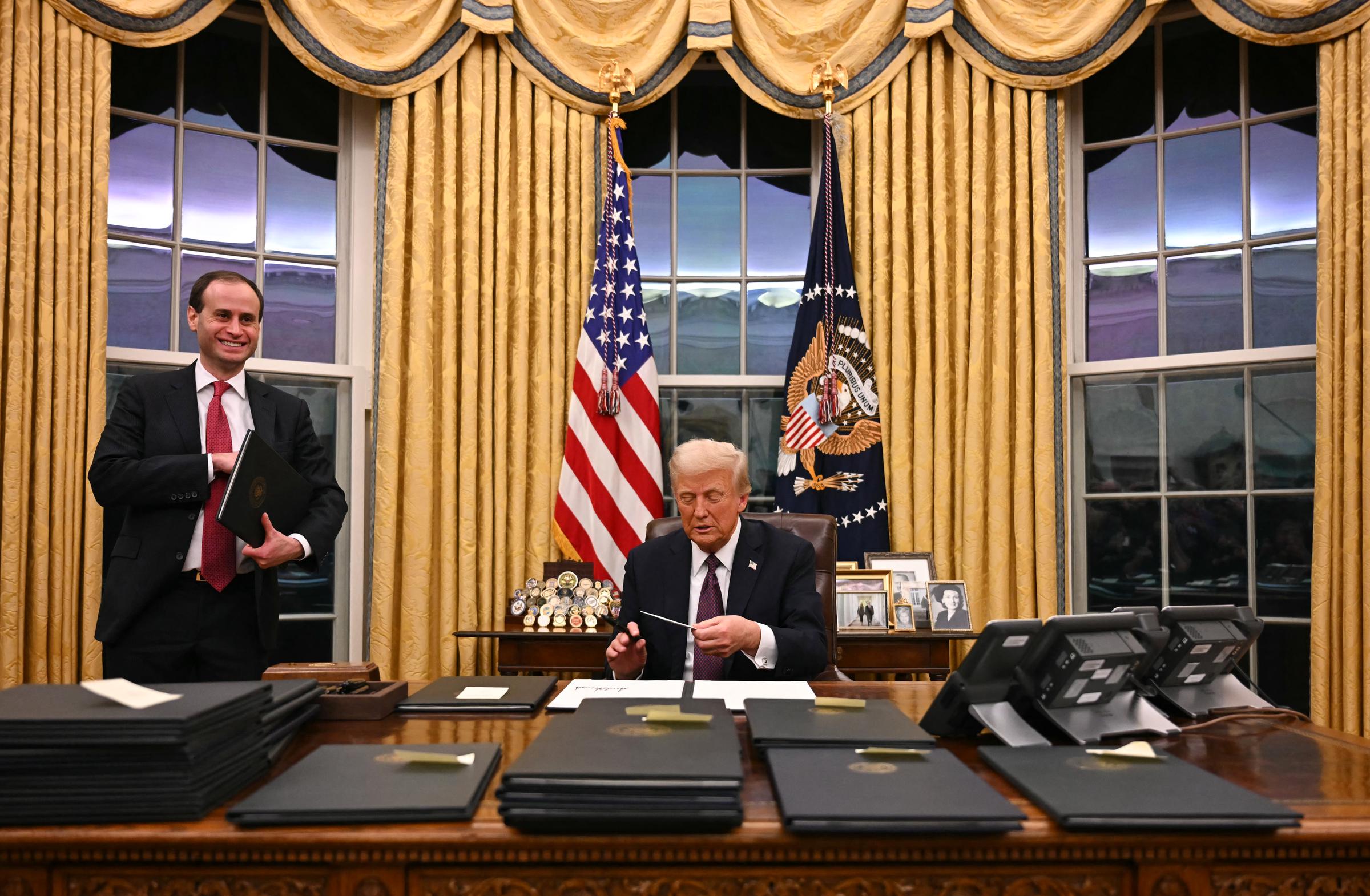 US President Donald Trump holds up outgoing President Joe Biden's letter as he signs executive orders in the Oval Office of the White House in Washington, DC, on January 20, 2025 | Source: Getty Images