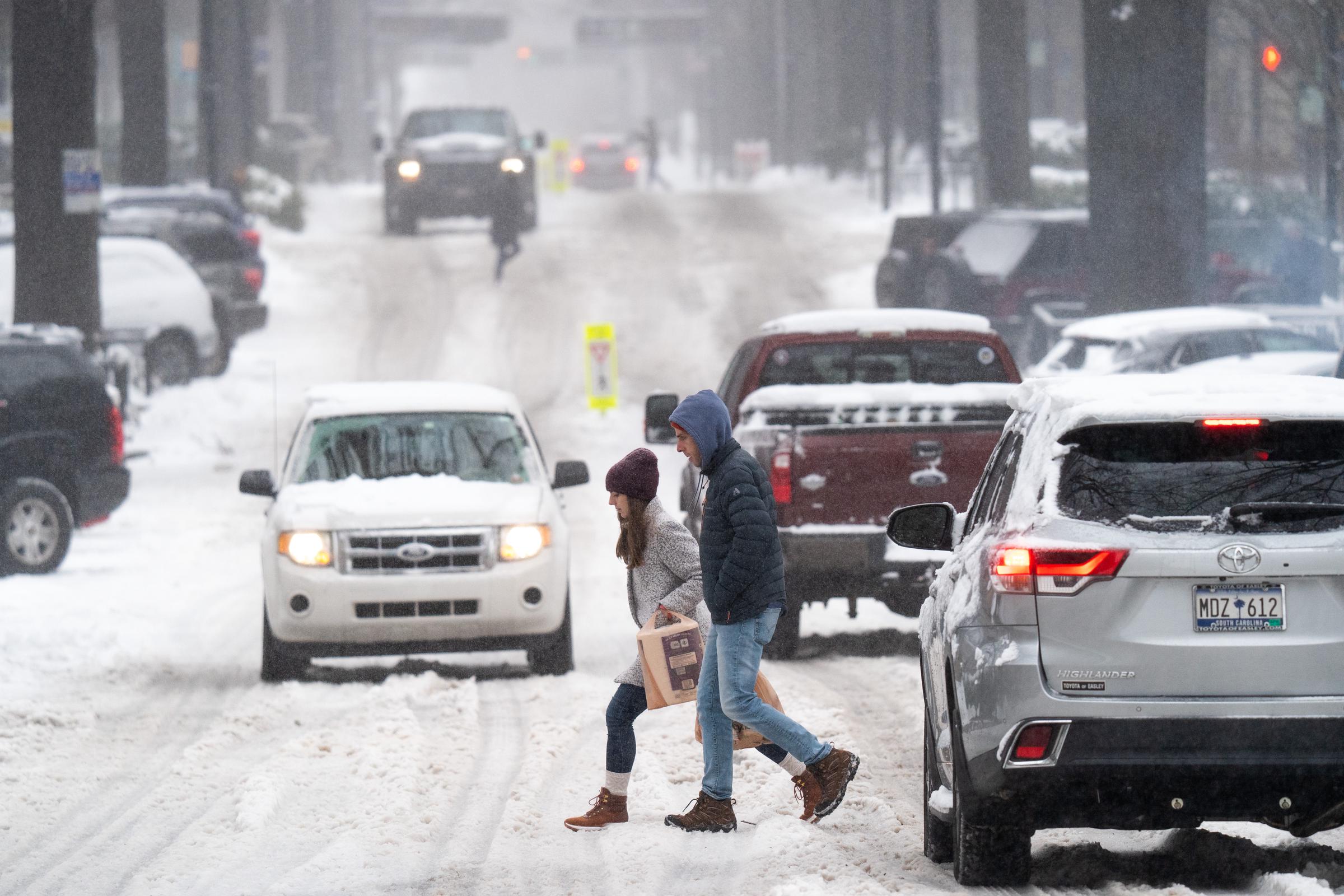 Pedestrians cross a street as motorists drive through the snow on January 16, 2022, in Greenville, South Carolina | Source: Getty Images