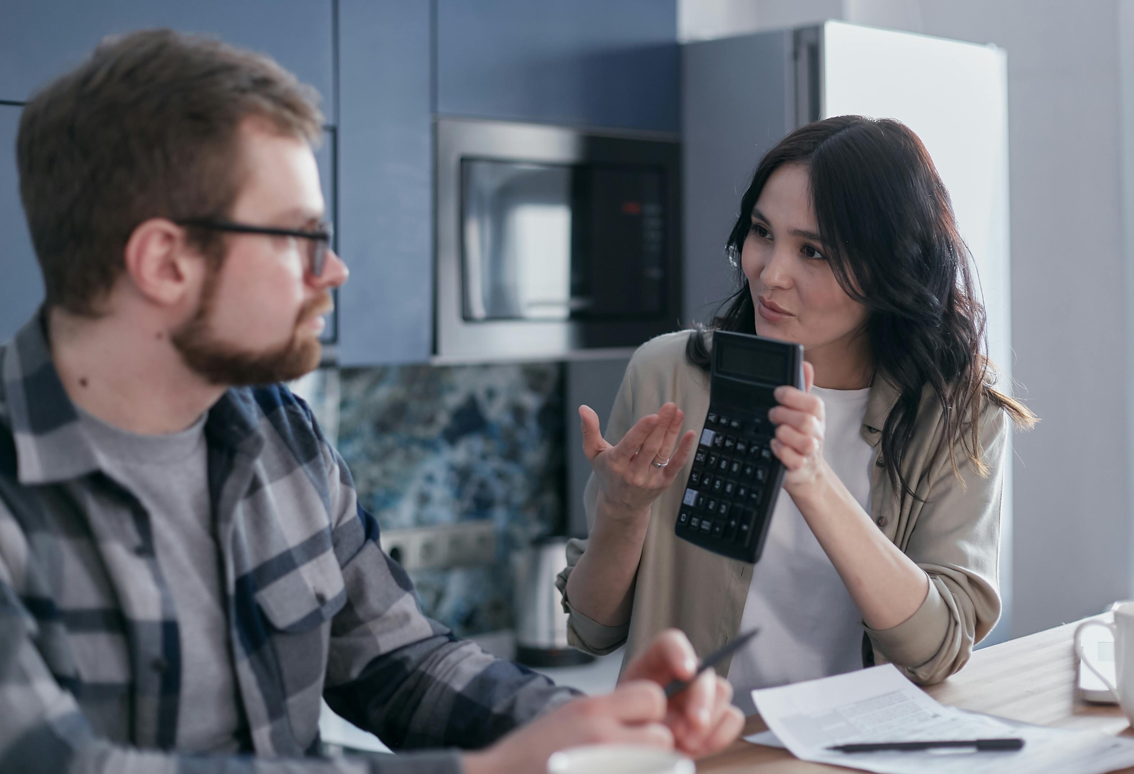 A man and a woman sitting at table as she shows him a calculator | Source: Pexels